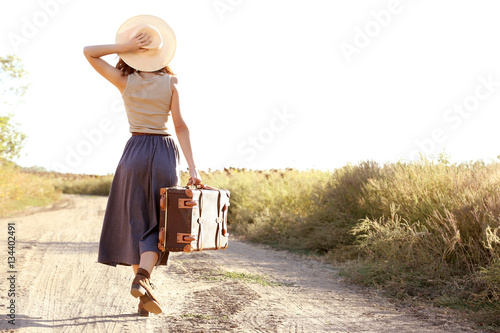 Young woman with suitcase walking along countryside road