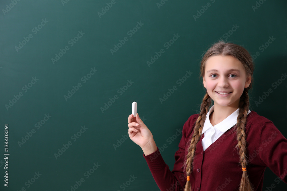 Teenage girl with piece of chalk  standing near green school blackboard
