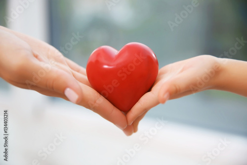 Hands of child and adult woman holding red heart  closeup