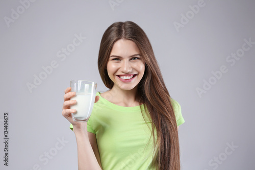 Beautiful young woman with glass of milk on grey background