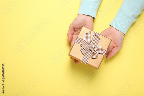 Female hands holding gift box, on color background