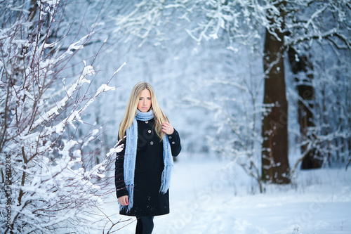 Attractive young blonde girl walking in winter forest. Pretty woman in wintertime outdoor. Wearing winter clothes.