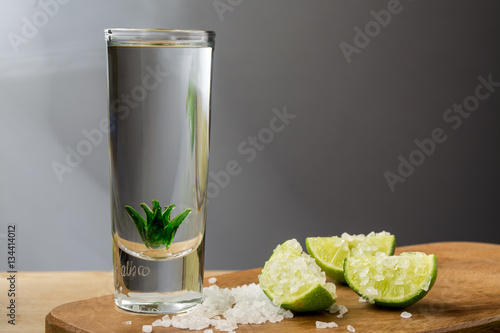 Tequila shot with limes and salt on wooden surface