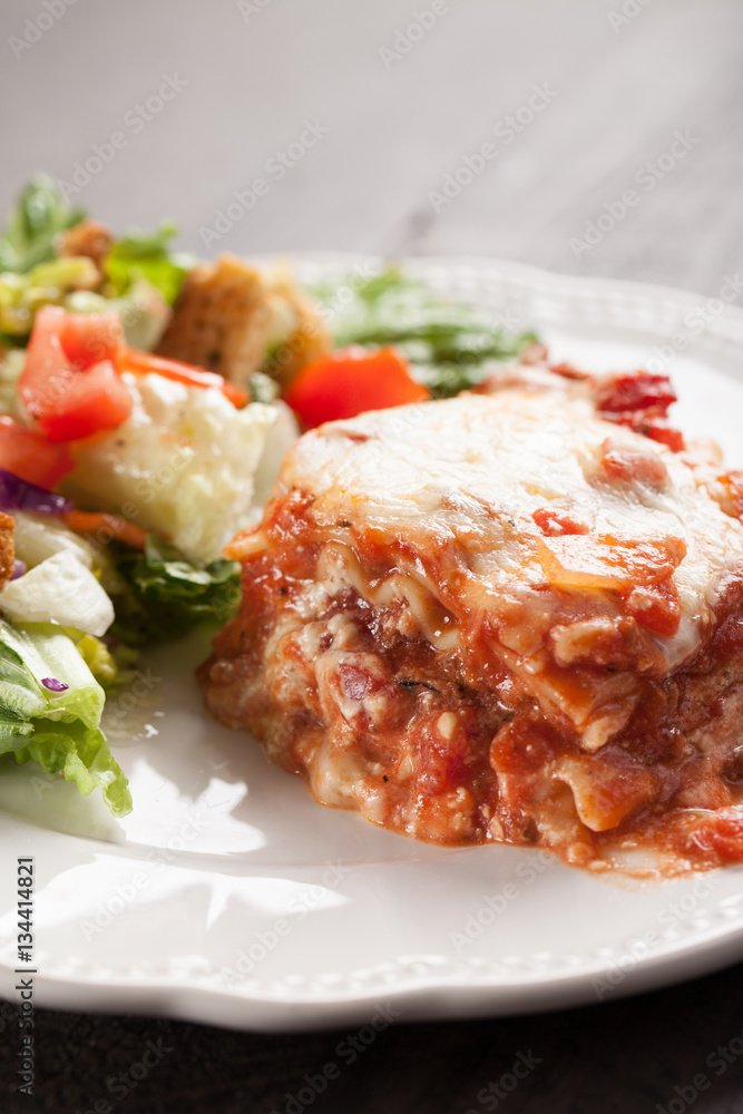 Homemade Italian four cheese lasagna with a side salad vertical shot