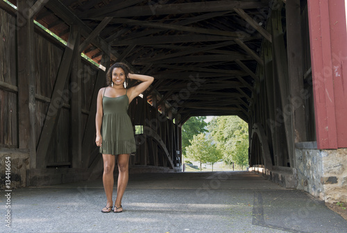 Stunning young biracial woman in green sundress standing in front of covered bridge