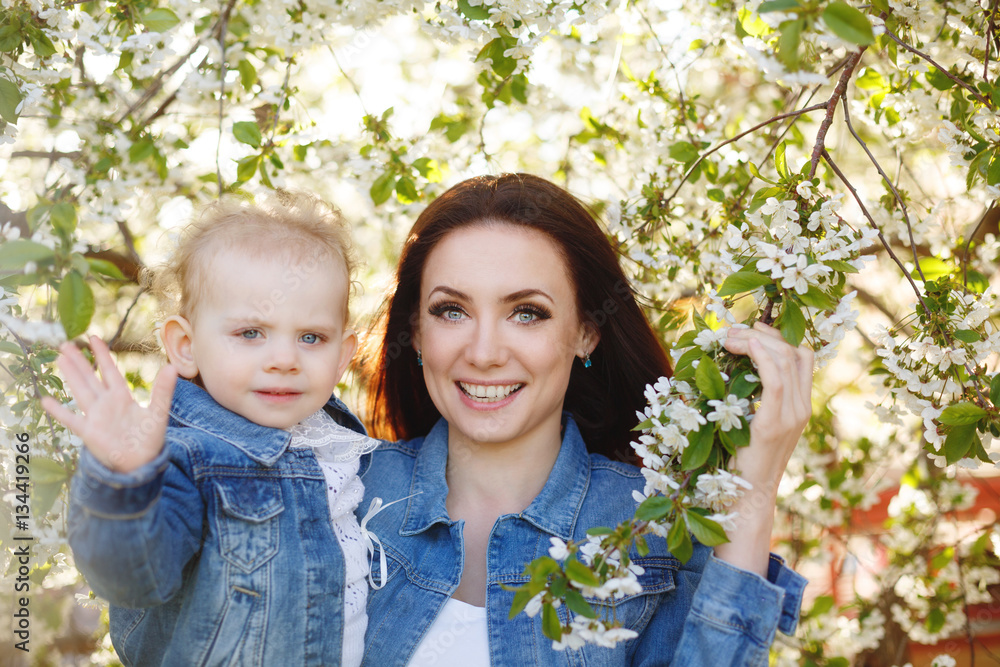 Mother and daughter on a background of a blossoming tree. Girls smile. Spring mood. Family time Mother and daughter on a background of a blossoming tree. Girls smile. Spring mood. Family time