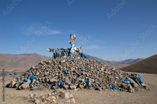 Ovoo made from stones worshipers have placed while praying. It is topped with a branch and many blue scarves and offerings.  photo