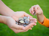 abstract money saving for family. kid hand is holding coins to put on or give to mother hands that holding another coins with green grass background