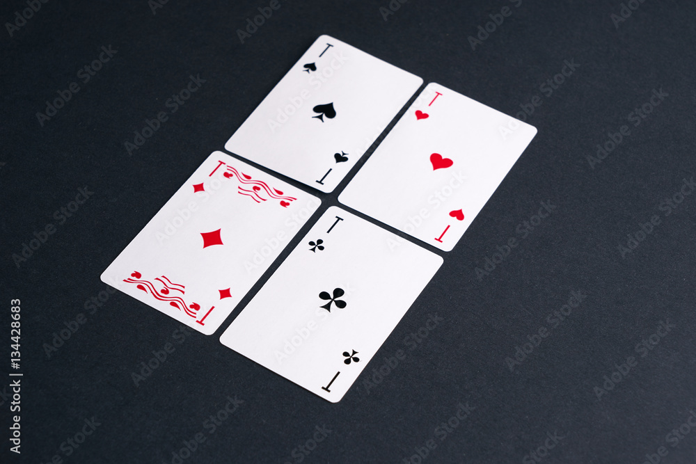 High Angle View of Four Playing Cards Spread Out on Dark Background Showing Aces from Each Suit - Hearts, Clubs, Spades and Diamonds