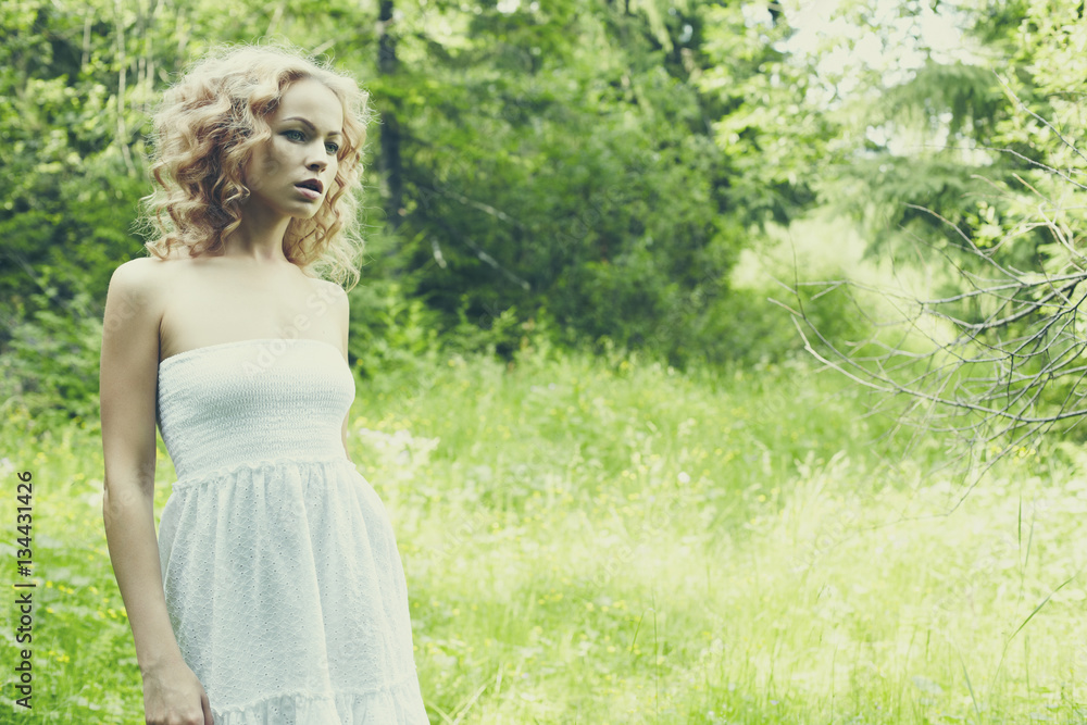 Beautiful young woman wearing elegant white dress standing in forest Beautiful young woman wearing elegant white dress standing in forest