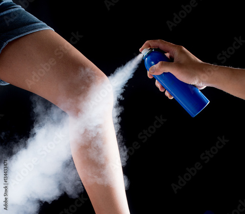 Analgesic spray can spraying on leg with black background,medica