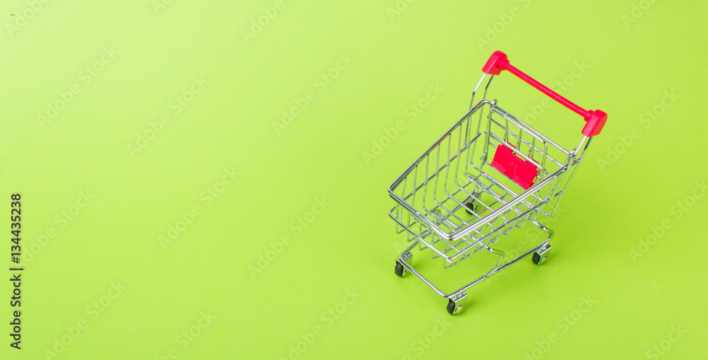 Empty shopping cart with the red handle on a green background