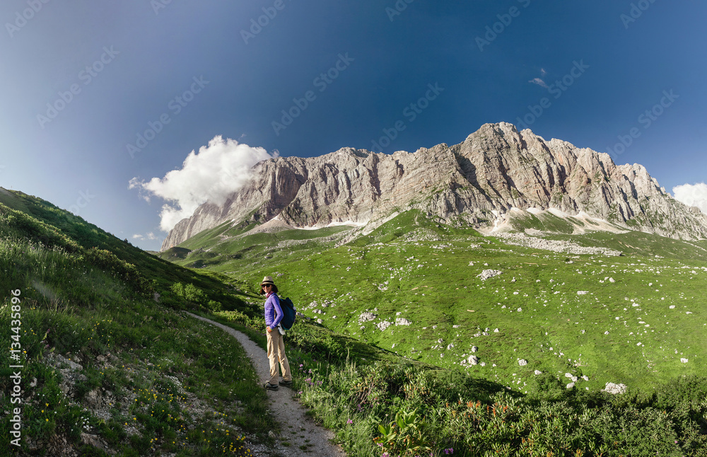 woman hiking on mountain trail on a meadow, rear view