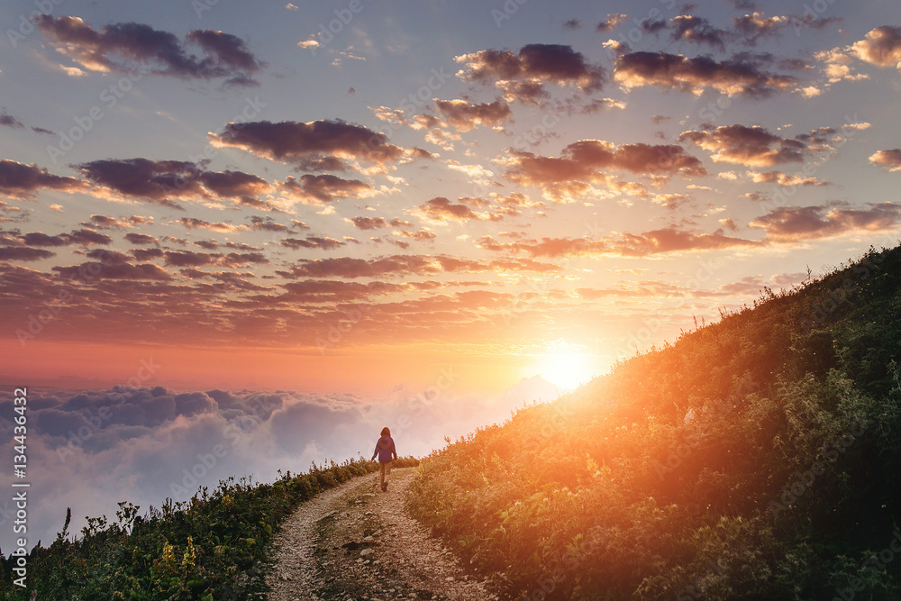 Obraz premium Kobieta podziwia zmierzch z chmurami i mgłą na śladzie.