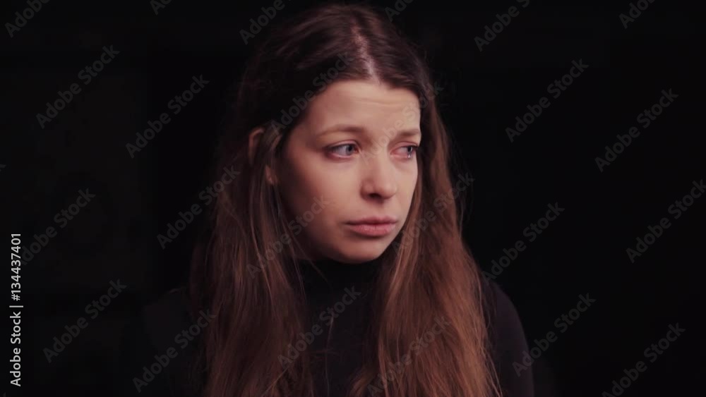 Close up view of a sad lonely young woman with a messy hair and tearful blue eyes on the black screen. The upset unhappy girl is trying to calm down, not looking towards the camera. Close up view of a sad lonely young woman with a messy hair and tearful blue eyes on the black screen. The upset unhappy girl is trying to calm down, not looking towards the camera.