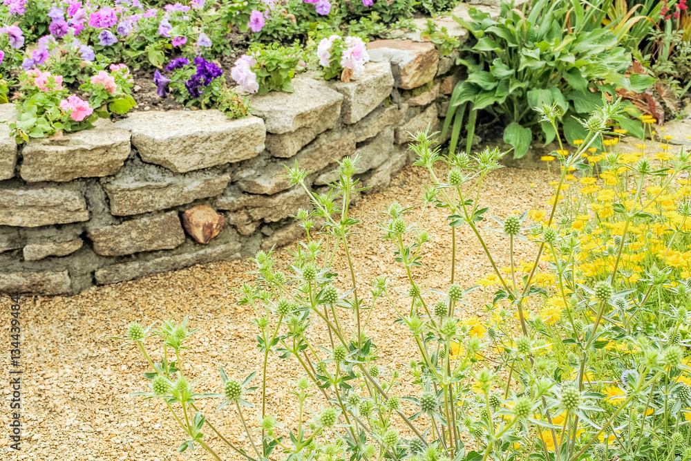 Naklejka premium Fragment of the alpine slide with a retaining wall and flowers