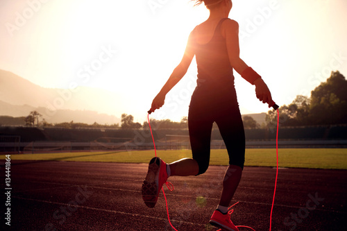 Young woman skipping rope during sunny morning on stadium track