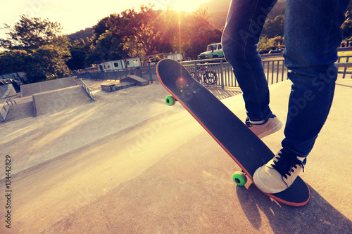 young skateboarder legs riding skateboard at skatepark