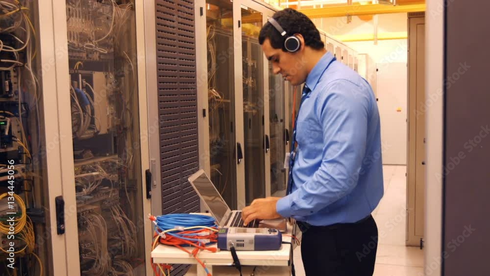 Technician talking on head phones while working laptop in server room 4k Technician talking on head phones while working laptop in server room 4k
