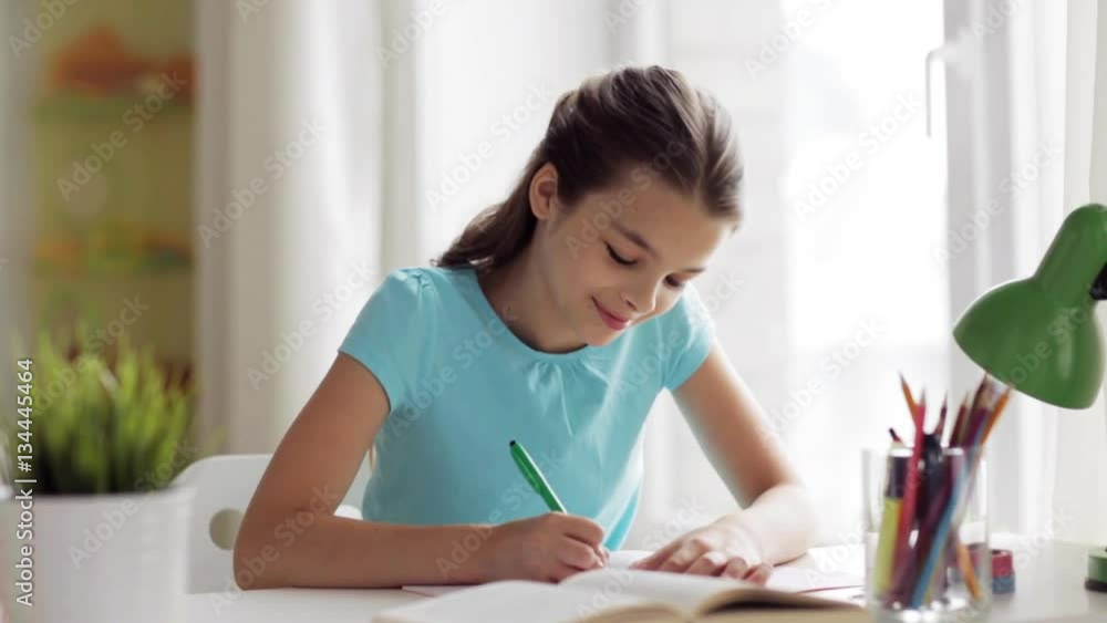 happy girl with book writing to notebook at home