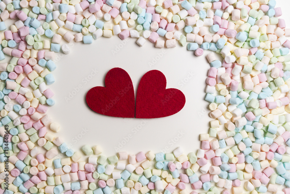 Obraz premium Two red hearts in the frame of colorful mini marshmallows as background