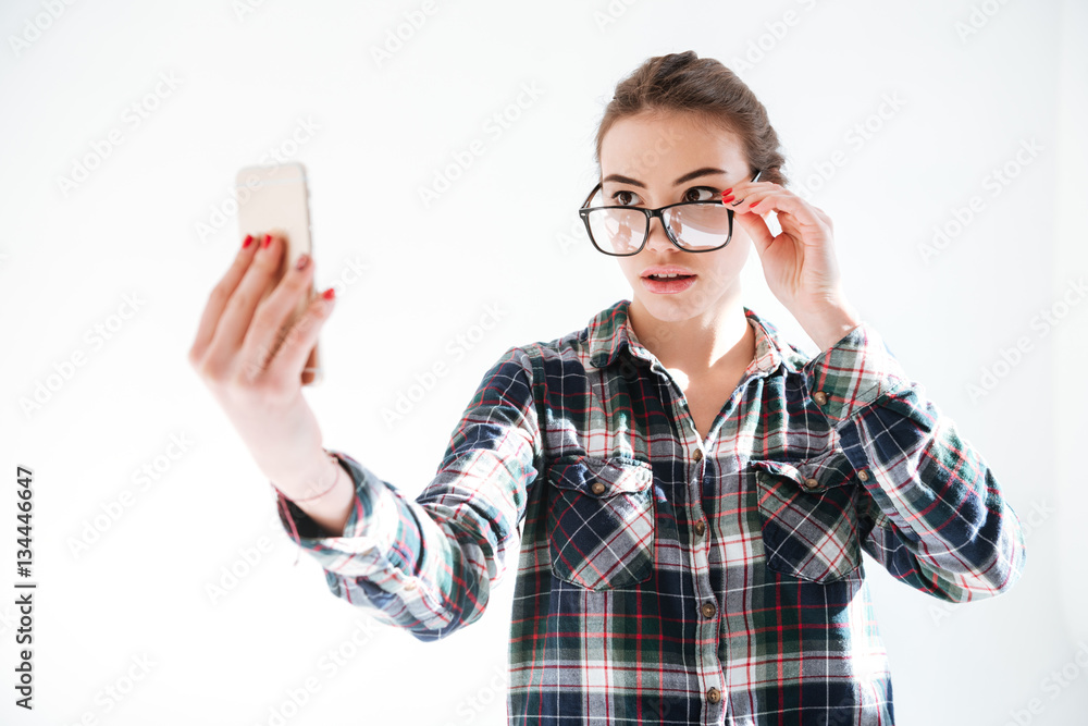 Woman looking over glasses and taking selfie with cell phone