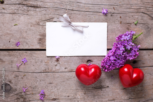 Empty tag, two red hearts and fresh violet lilac flowers on age