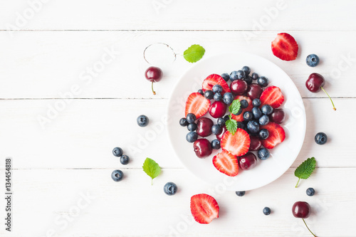 Schilderij op canvas Fruit salad with strawberry, blueberry, sweet cherry on wooden white background
