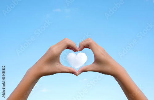 Asian young girl hands  holding hands in heart shape framing on cloud heart shape with clear blue sky background for Happy valentines day or wedding concept and copy space.