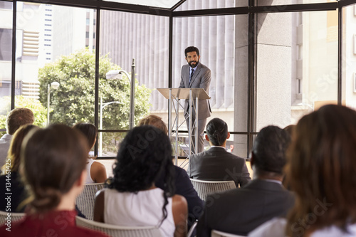 Tablou pe pânză Hispanic man presenting business seminar leaning on lectern