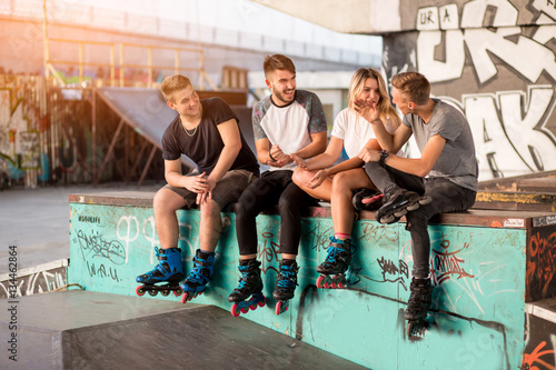 Young people on rollerblades sitting. Girl and guys in skatepark. Listen to the friend's story.