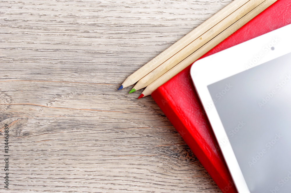 Obraz premium Red diary notebook, white tablet and colored pencils on desk woo