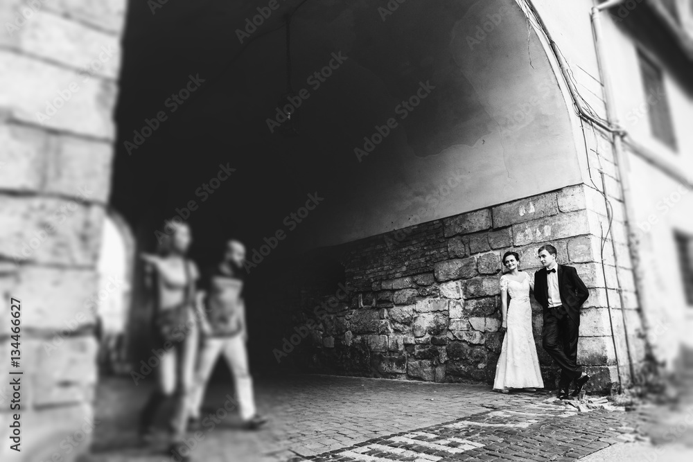 People pass wedding couple standing before the wall
