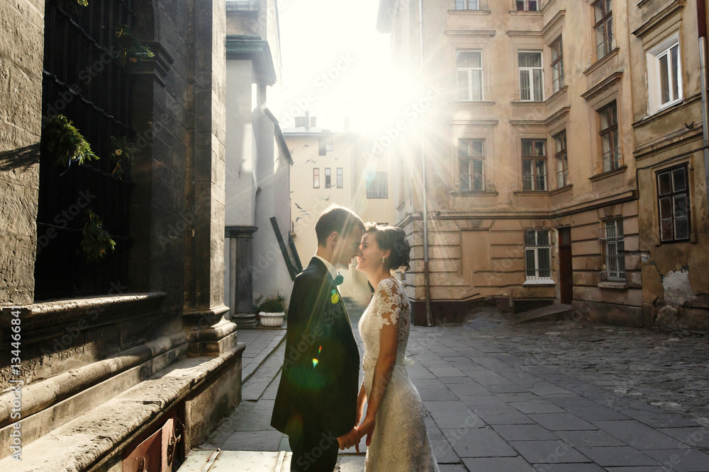 Smiling bride holds groom's hands standing in the rays of mornin Smiling bride holds groom's hands standing in the rays of mornin