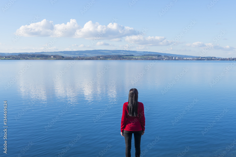 On the other side. Woman stands on the lake shore at the water's edge. On the sky light clouds. Further prospects.