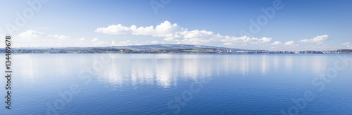 Clear day. Lake Zug in central Switzerland. Clouds are reflected in water lake. At the edge water is clear and see the bottom of the lake.