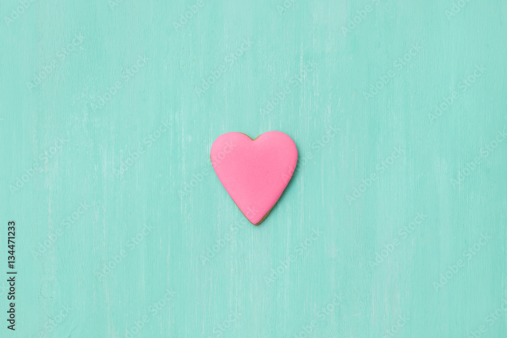 Top view on a little gingerbread cookie in shape of heart on light blue background. Flay layout. Love, Valentines's day concept Top view on a little gingerbread cookie in shape of heart on light blue background. Flay layout. Love, Valentines's day concept