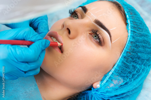 Cosmetologist making permanent makeup on woman's face