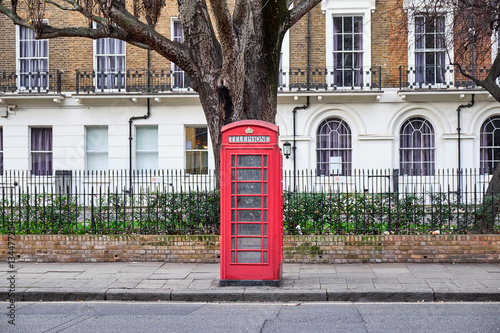Iconic red London phone booth in front of a block of residential building and a big tree in the Paddington area