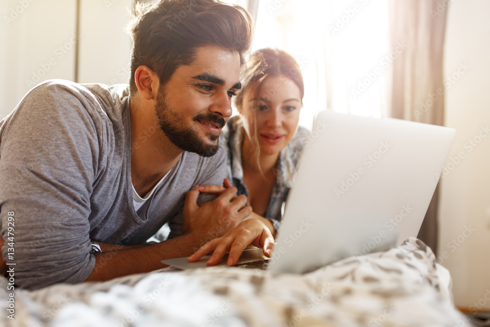 Young married couple lying on bed at home and using laptop. Young married couple lying on bed at home and using laptop.