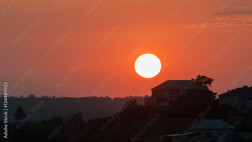 The sun sets on the background of the rural house. Red, orange sunset, landscape. The sun sets on the background of the rural house. Red, orange sunset, landscape.