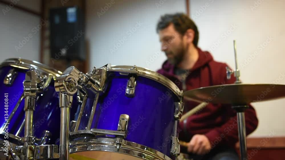 Drum set in studio, focus on toms, drummer playing instrument out of focus in background Drum set in studio, focus on toms, drummer playing instrument out of focus in background