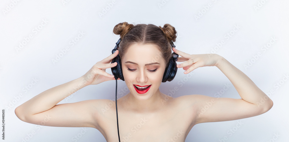 Young pretty woman trendy makeup bright red lips bun hairstyle bare shoulders act the ape with big dj headphones on white studio background Young pretty woman trendy makeup bright red lips bun hairstyle bare shoulders act the ape with big dj headphones on white studio background