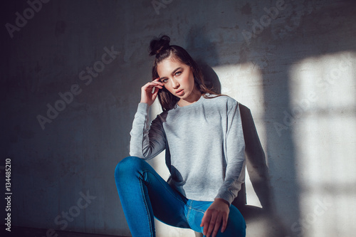 Beautiful girl dressed in blank sweatshirt sitting on a gray background. Mock-up.