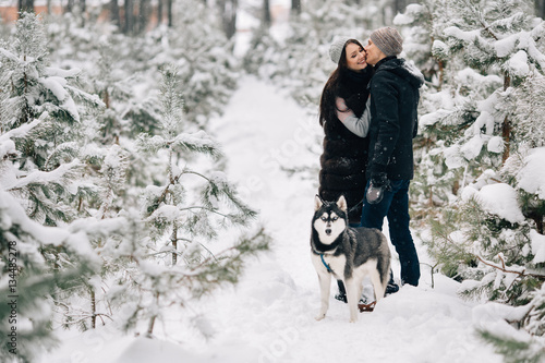 Beautiful couple in love and Siberian husky dog walking in snowy pine winter forest © Maksym Azovtsev