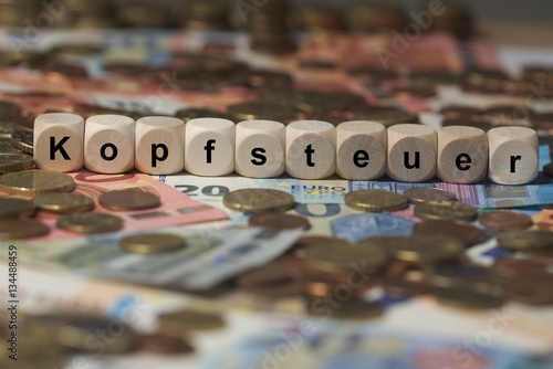 kopfsteuer - Holzwürfel mit Buchstaben im Hintergrund mit Geld, Geldscheine photo