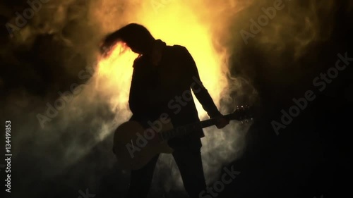 Silhouette of a girl with a guitar in the smoke. Strobe lights, smoke machines. Concert rock band,  guitar. Music video, heavy metal or rock group. Slow motion.  photo