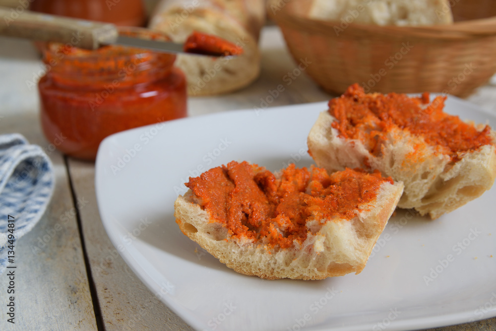 Some typical sobrassada from Majorca spreaded on rustic bread. Meal served on a white wooden table in a rustic kitchen. Some typical sobrassada from Majorca spreaded on rustic bread. Meal served on a white wooden table in a rustic kitchen.