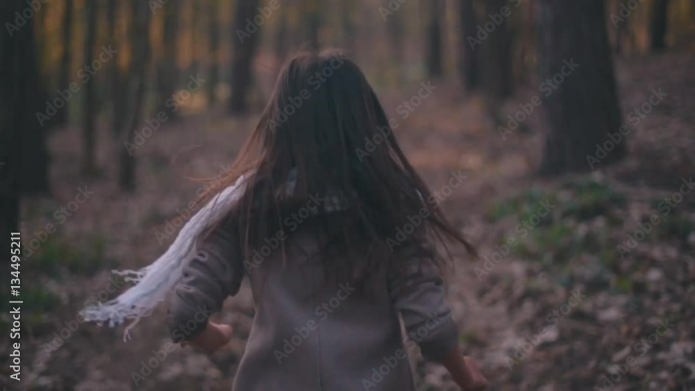 Small teenage girl with long brunette hair and stylish look. Scared little girl running in the forest, she looks around terrified as something is following her. Deserted scary forest, nightmare.