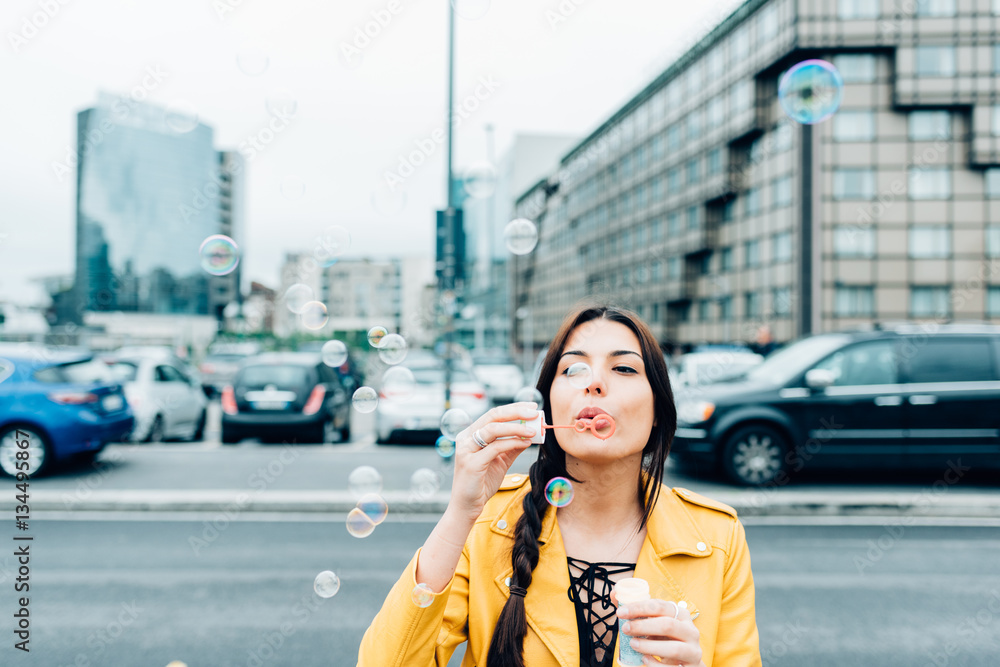 young beautiful yellow dressed vintage hipster woman outdoor in the street of the city playing with bubble soap - childhood, having fun, happiness concept